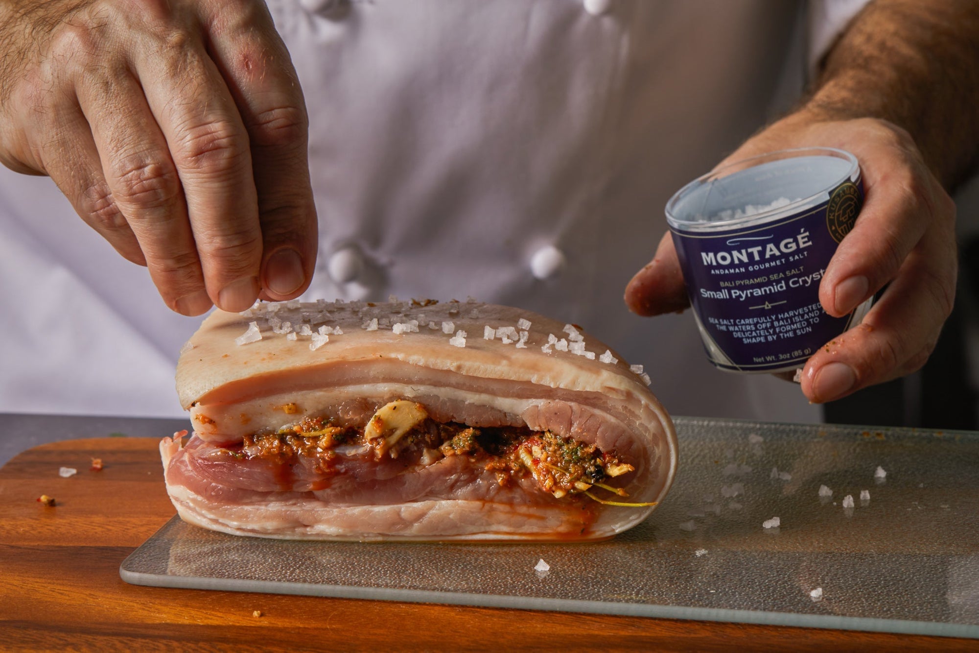 Chef seasoning a stuffed pork belly roll with Montagé Bali Pyramid Sea Salt before cooking