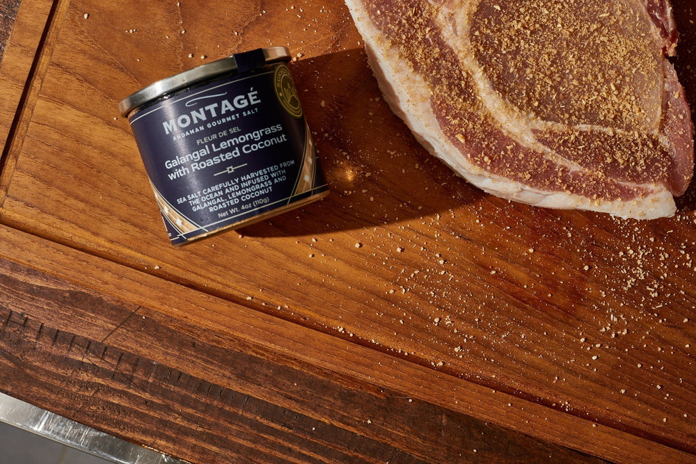 Montagé Sukhothai finishing salt tin next to a seasoned raw pork chop