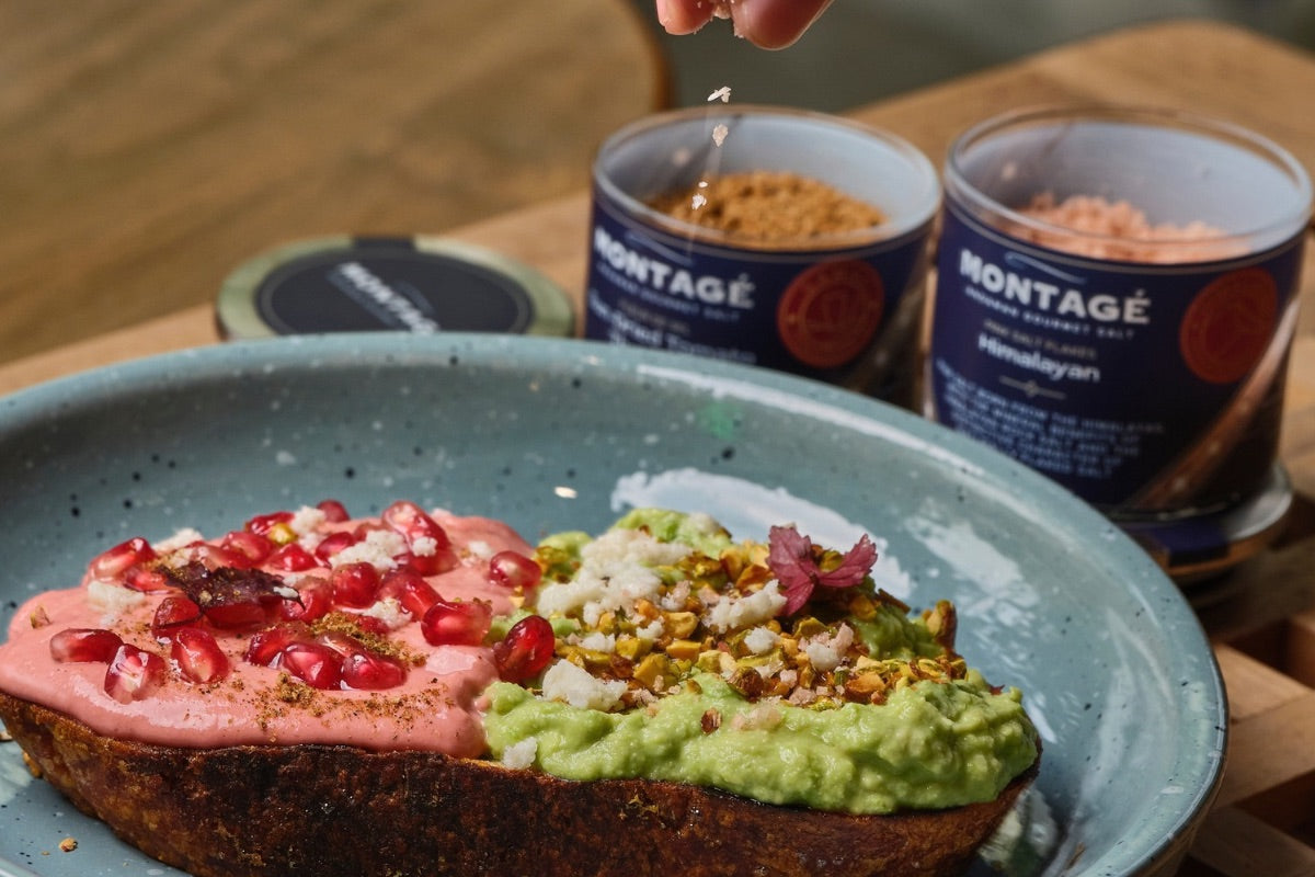 Pinching Himalayan salt flakes over avocado toast topped with pomegranate and pistachio