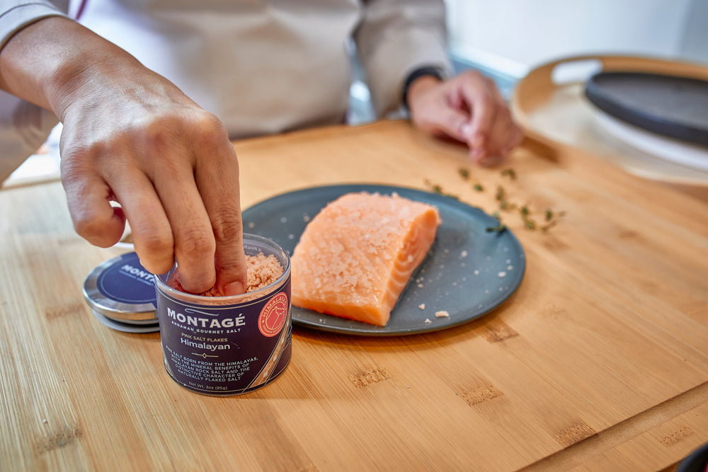 Pinching Montagé Himalayan pink flaky salt over a raw salmon fillet
