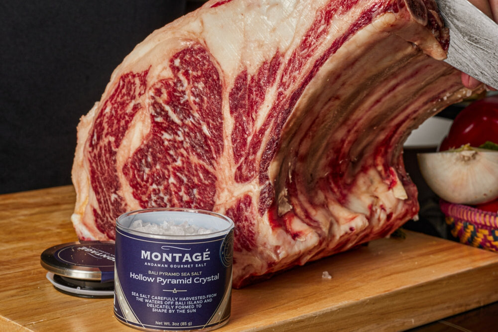 Raw bone-in prime rib roast with a tin of Montagé Tejakula hollow pyramid sea salt on a wood cutting board