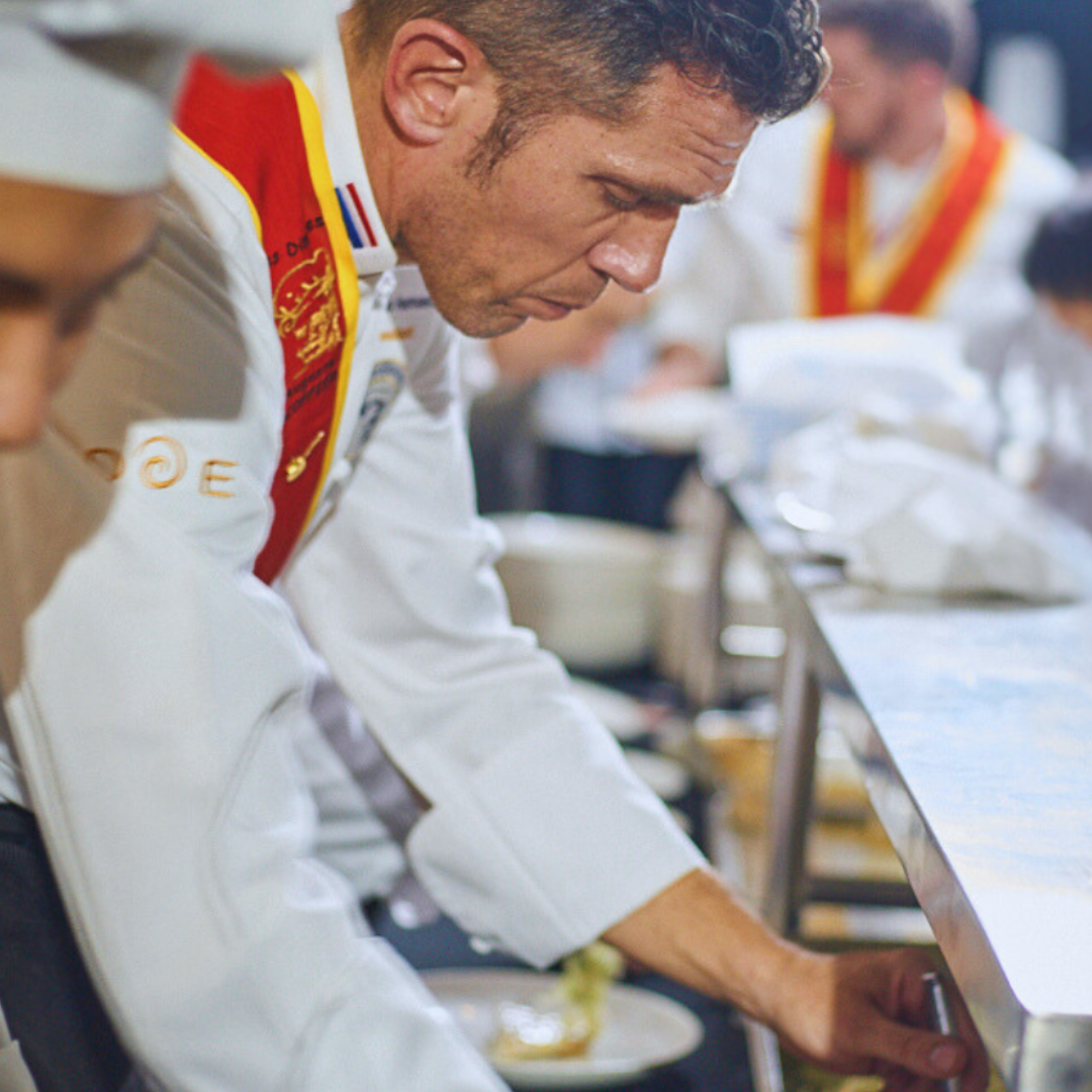 Disciples Escoffier International in a kitchen preparing food, with one chef focusing on plating up with salt.