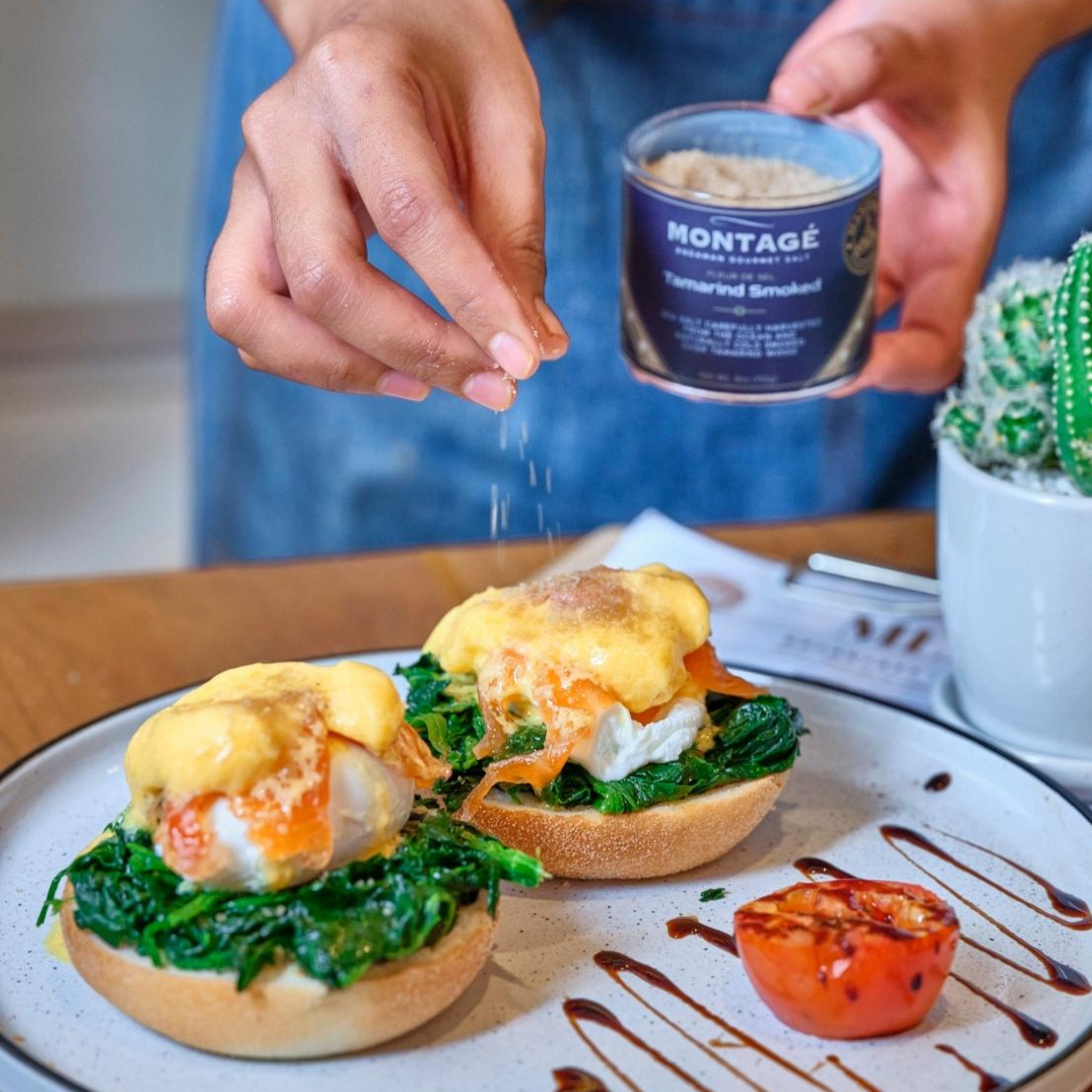 Person seasoning food on a plate with Montage seasoning, surrounded by a cactus plant.
