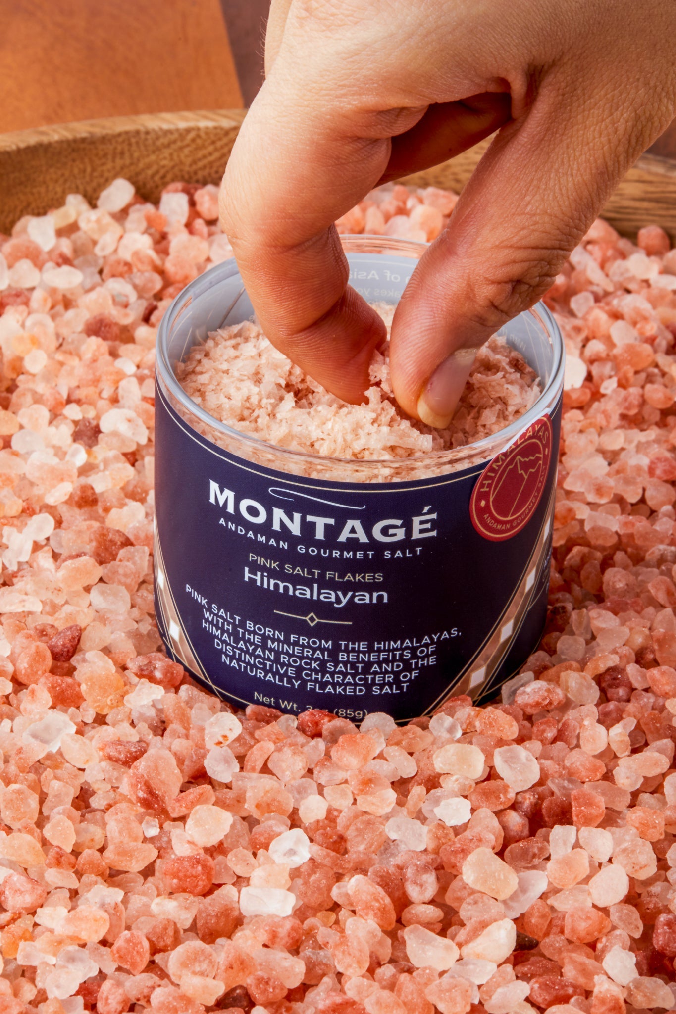 Jar of Montagé Himalayan pink flake salt nested in raw Himalayan rock salt crystals showing the naturally flaked texture