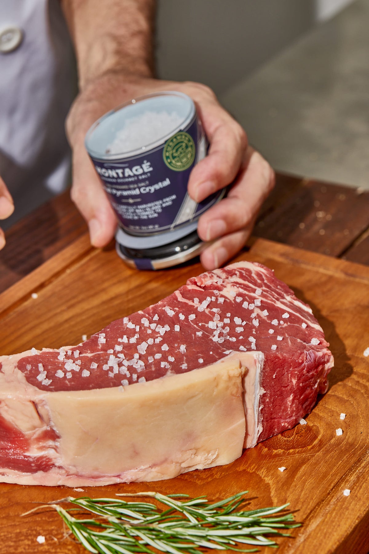 Montagé Kusamba pyramid sea salt jar held over a raw strip steak on a wood board