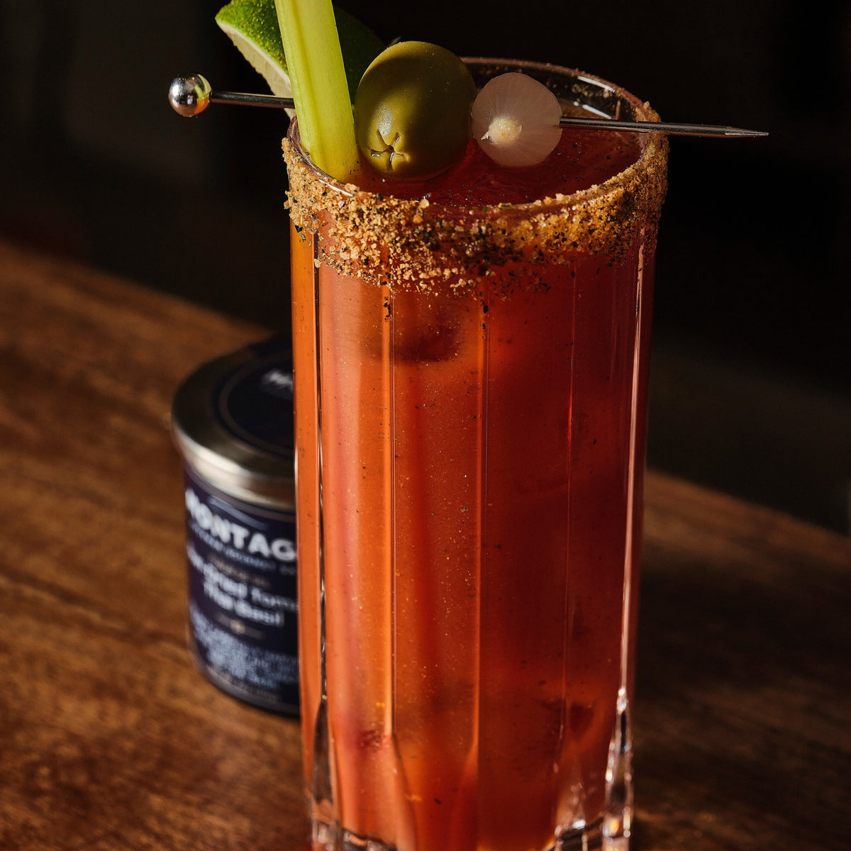 Bloody Mary in a mason jar with a Montagé Roasted Garlic Sweet Onion salt rim, celery and lemon, beside the open jar