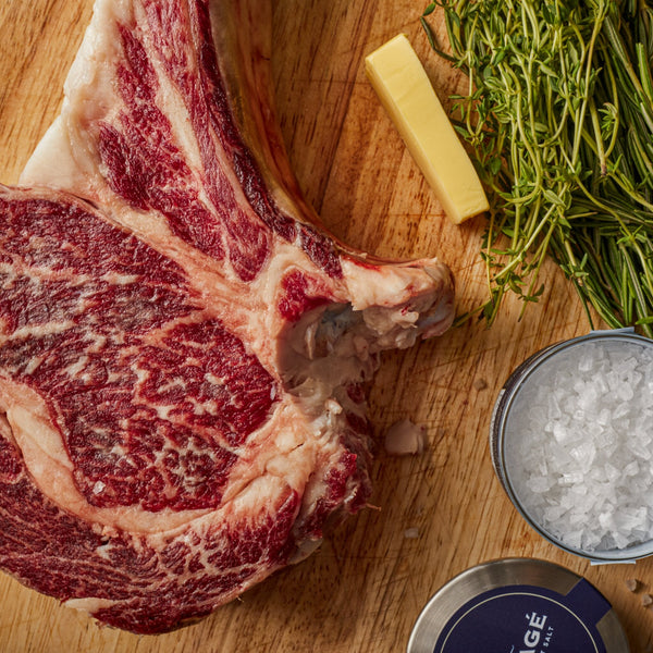 Raw bone-in ribeye steak with butter, herbs, garlic, and Montagé Tejakula hollow pyramid salt
